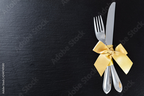 fork and knife with golden ribbon on slate tray