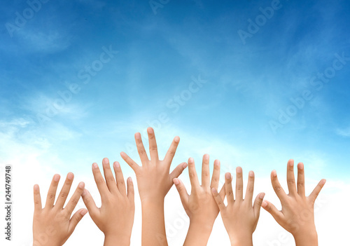 children raised up hands on blue sky with clouds