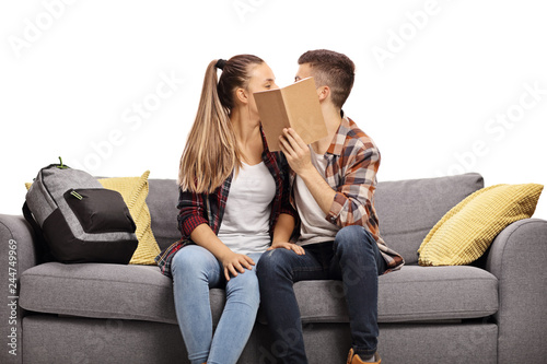 Teenage couple kissing and hiding behind a book