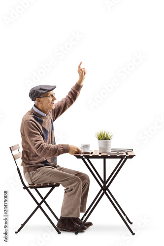 Senior man sitting at a coffee table and gesturing to call a waiter