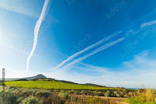 Contrails over a green hill at sunset