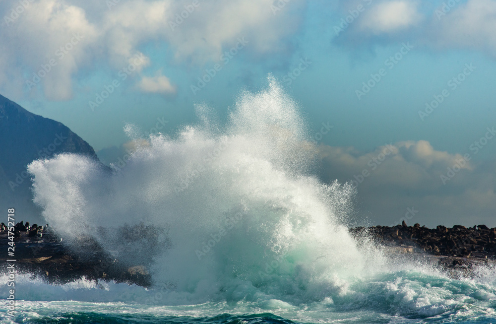 Big waves break on the rocks in the sea against the backdrop of the coastline. Beautiful seascape.  A beautiful moment. Very dynamic photo. Cape Town. False Bay. South Africa.