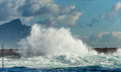 Big waves break on the rocks in the sea against the backdrop of the coastline. Beautiful seascape. A beautiful moment. Very dynamic photo. Cape Town. False Bay. South Africa.