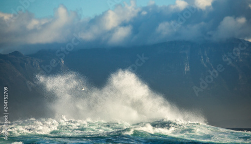 Fototapeta Naklejka Na Ścianę i Meble -  Big waves break on the rocks in the sea against the backdrop of the coastline. Beautiful seascape.  A beautiful moment. Very dynamic photo. Cape Town. False Bay. South Africa.