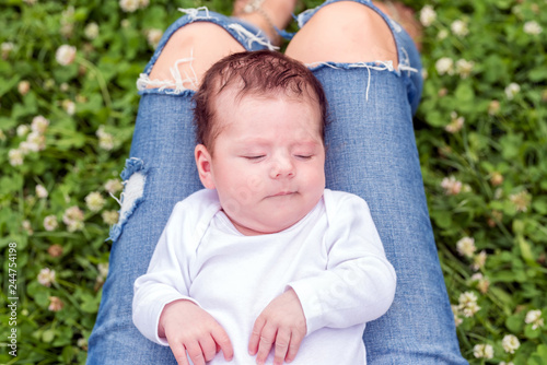 Portrait of a baby girl lying on her mothers lap while she is lying on the grass in the park.