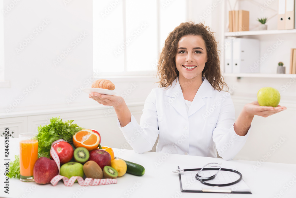 Woman nutritionist holding fruit and croissant in hands