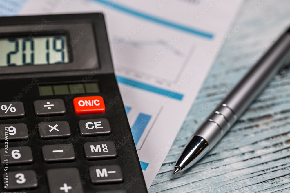 Calculator with 2019 digits lie on financial document with pen on the wooden table Calculator with 2019 digits lie on financial document with pen on the wooden table