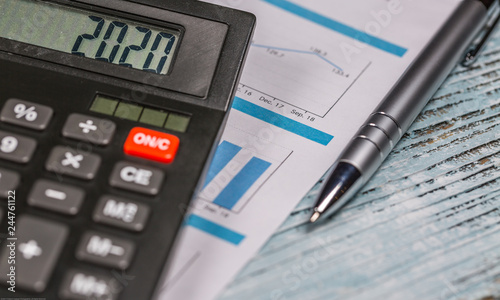 Calculator with 2020 digits lie on financial document with pen on the wooden table