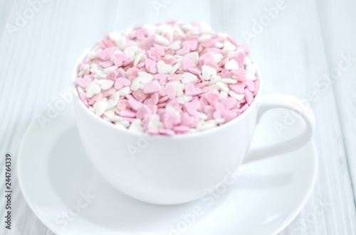 White coffee cup on wooden floor.Many small hearts, white and pink, are in a cup of coffee.