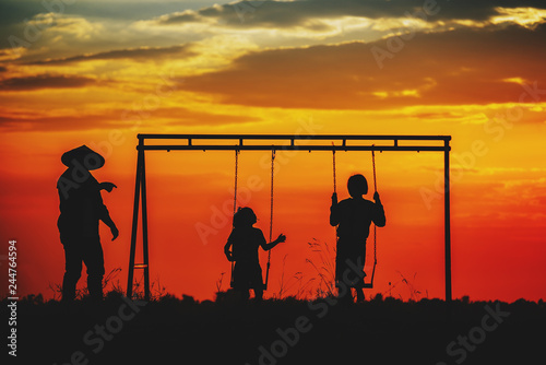 Silhouette of happy Family on sunset background,Father and two daughters are enjoying playing swings,Funny family concept