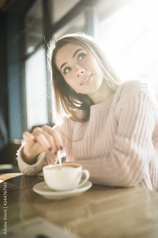 Young pretty woman holding coffee spoon and stirring hot coffee on wooden table.