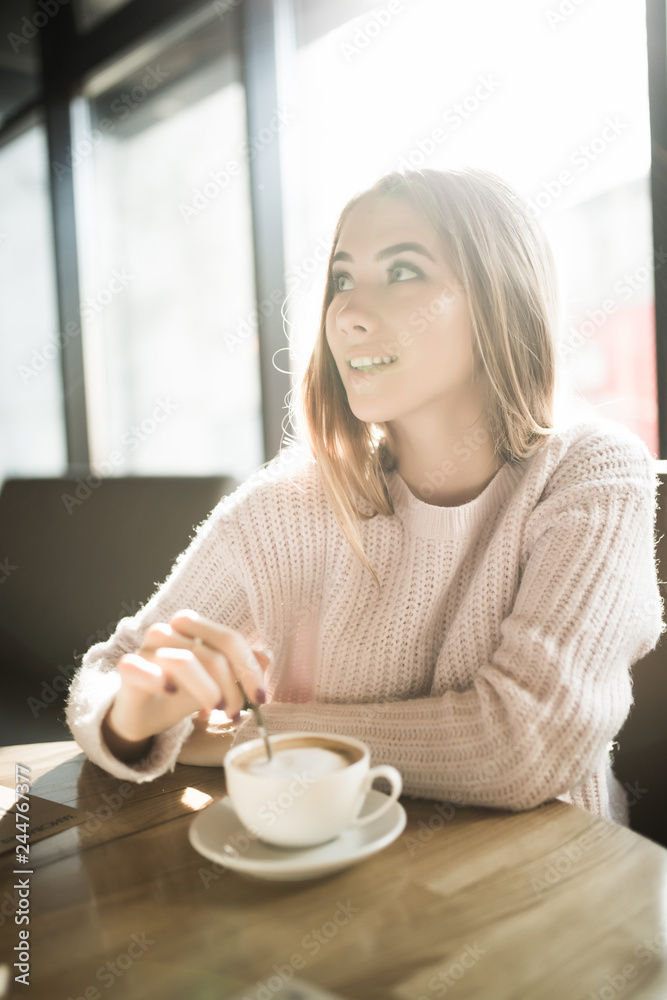 Young pretty woman holding coffee spoon and stirring hot coffee on wooden table Young pretty woman holding coffee spoon and stirring hot coffee on wooden table