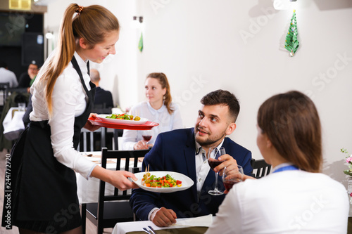 Welcoming female waiter is serves the dish to client in restaurante