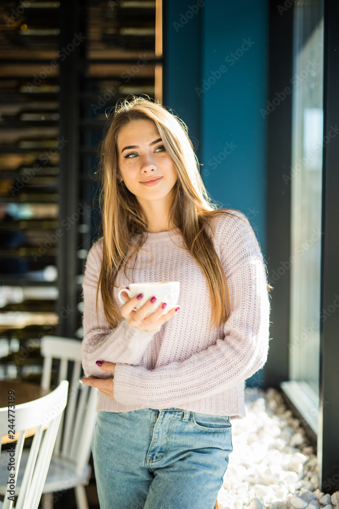 Young and pretty woman standing with cup of coffee in cafe