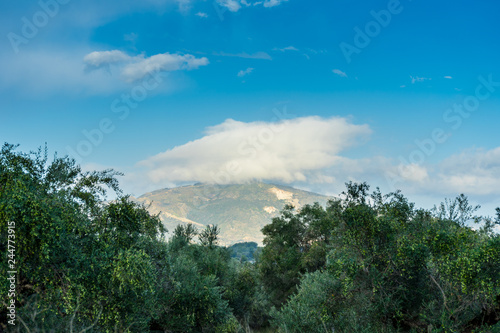 Greece, Zakynthos, Magic glowing cloud hanging over green mountain behind olive grove © Simon