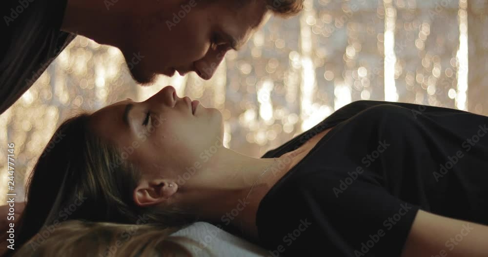 A sweet moment as a young woman sleeps and her boyfriend gives her gentle upside kiss on the forehead and nose, she wakes and smiles and they kiss