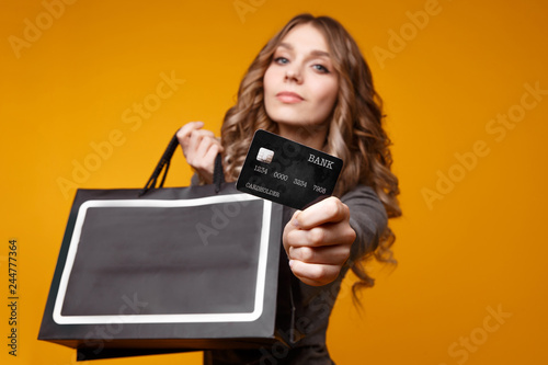 lose-up portrait of happy young brunette woman holding credit card and black shopping bags, looking at camera, isolated on yellow background photo