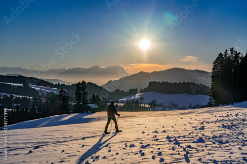 senior woman, snowshoeing in sunset in the Bregenzer Wald area of Vorarlberg, Austria with spectacular view on Mount Saentis, Switzerland