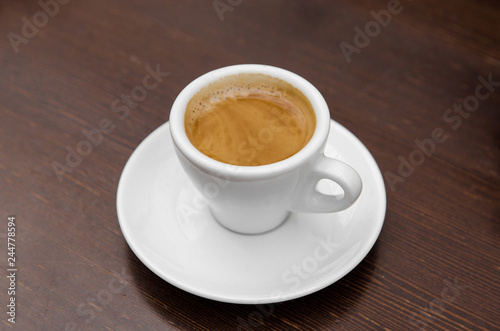 White cup with coffee on a white saucer on a wooden table