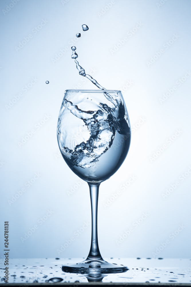 Splashing water on blue background. Wine glass with water. Splashing water on blue background. Wine glass with water.
