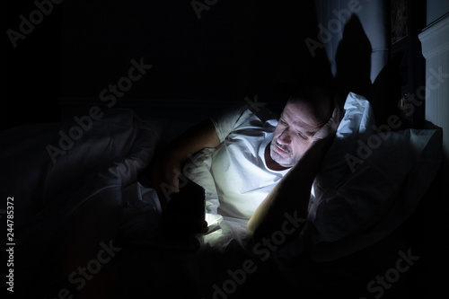 Man using his phone in his bed instead of sleeping, technology addiction concept