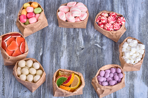 Colored candy in paper bags on wooden background