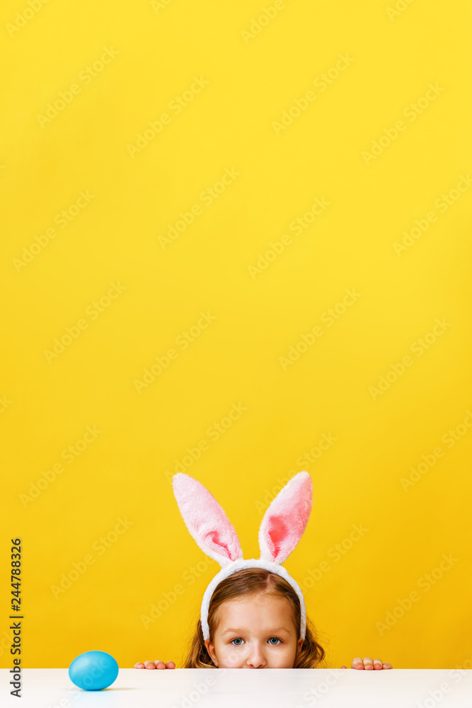 Fototapeta premium Cute little child girl with bunny ears at home is hunting for Easter eggs.
