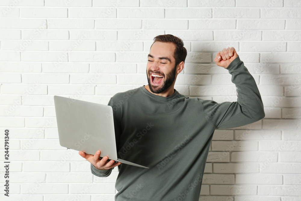 Emotional young man with laptop celebrating victory near brick wall Emotional young man with laptop celebrating victory near brick wall