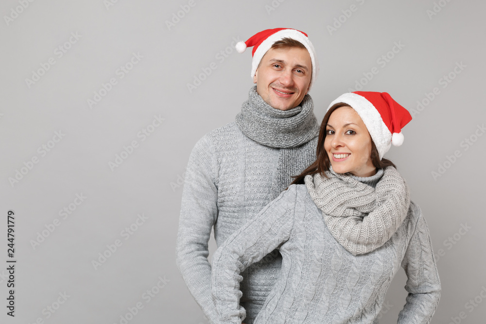 Merry fun couple girl guy in red Santa Christmas hat gray sweaters scarves isolated on grey wall background, studio portrait. Happy New Year 2019 celebration holiday party concept. Mock up copy space. Merry fun couple girl guy in red Santa Christmas hat gray sweaters scarves isolated on grey wall background, studio portrait. Happy New Year 2019 celebration holiday party concept. Mock up copy space.