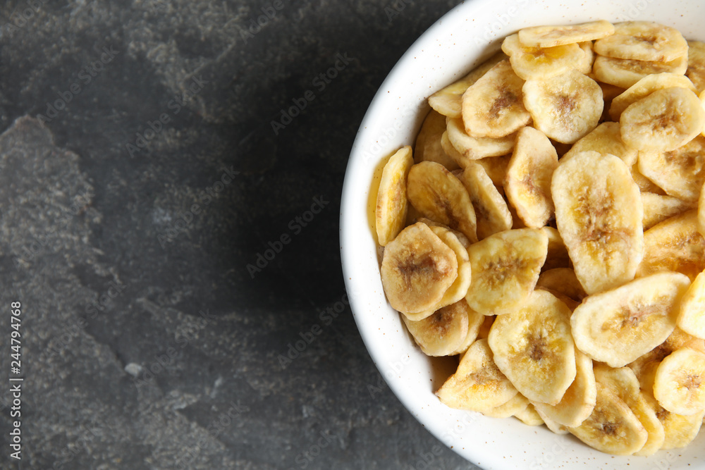 Bowl with sweet banana slices on grey background, top view with space for text. Dried fruit as healthy snack Bowl with sweet banana slices on grey background, top view with space for text. Dried fruit as healthy snack