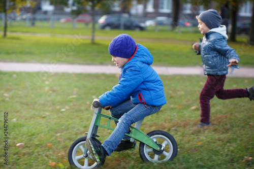 One child rolls on a runner and the second is catching up with him in the autumn park.