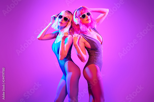 Fashion. Two sexy DJ girl in Colorful neon light dance. Glamour party fitness woman with Dyed Hair in Trendy headphones. Young beautiful model enjoy nightlife. Creative art style
