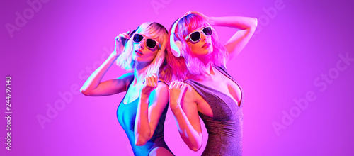 Fashion. Two DJ girl with Dyed Hair in Colorful neon light enjoy music, friends. Party disco 80s 90s vibes. Model woman in fashionable bodysuit, makeup. Creative art banner