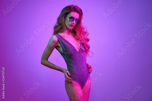 Sexy girl dance in glamour bodysuit with Trendy Fashion wavy hairstyle. Party Disco vibes. Young woman in Stylish sunglasses. Bright Pink Purple neon light. Art Color.