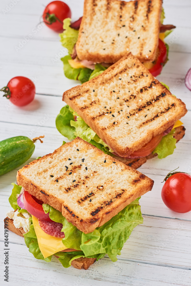 Three sandwiches with ham, lettuce and fresh vegetables on a white background Three sandwiches with ham, lettuce and fresh vegetables on a white background