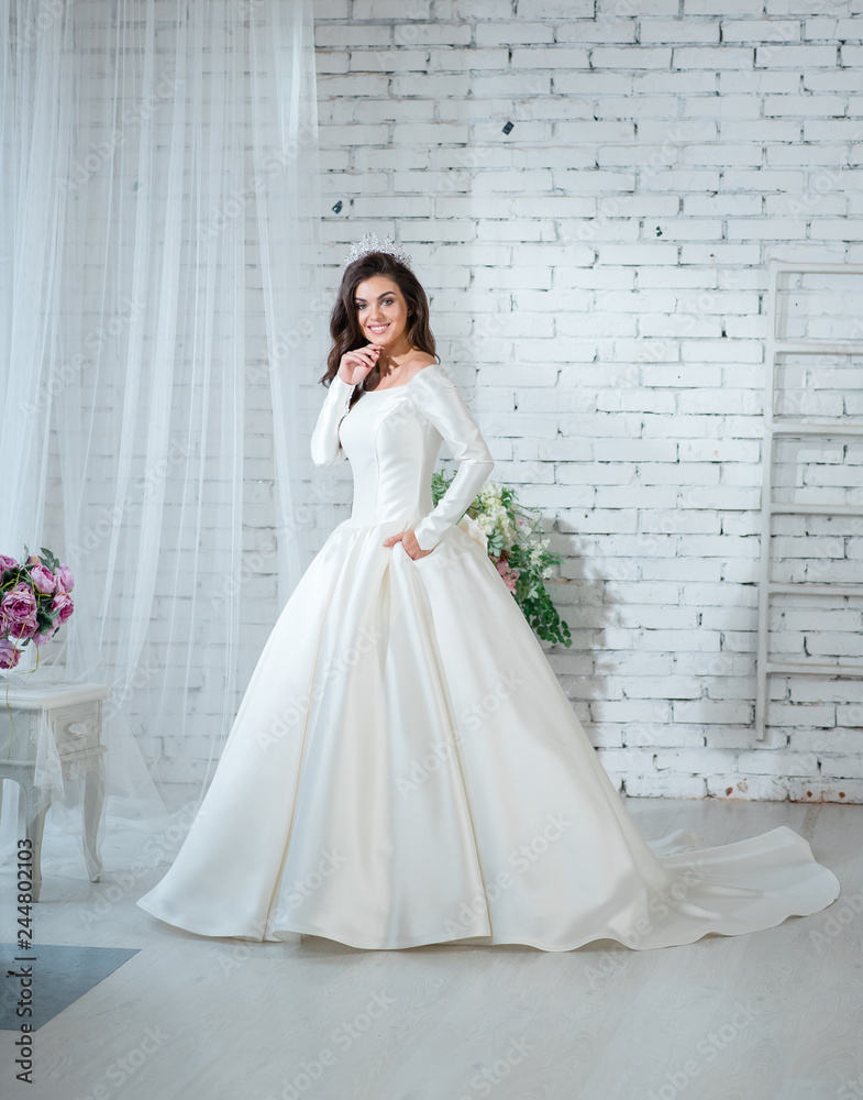 Portrait of beautiful bride woman in gorgeous white wedding dress posing in the bright studio with wedding decoration.