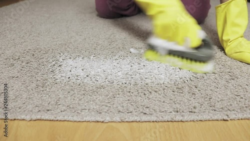 Woman in yellow rubber gloves cleaning carpet with a brush and foam