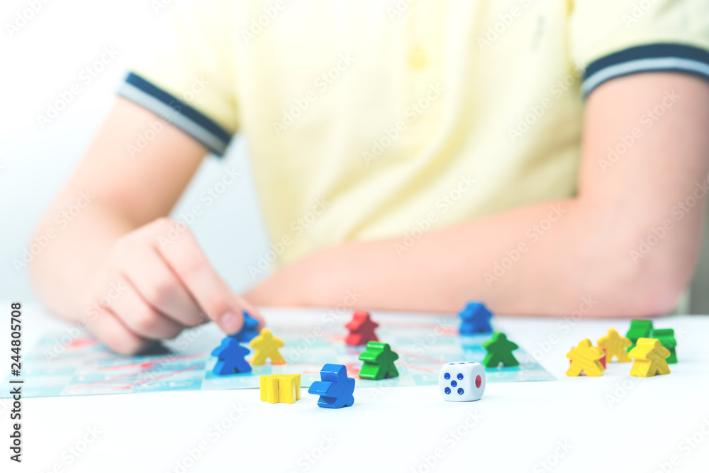 Child plays a board game with colorful pieces and a dice on tabletop Child plays a board game with colorful pieces and a dice on tabletop