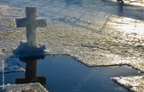 Cross christian symbol made from a block of ice on top of the ice on the frozen lake with cross shaped water hole