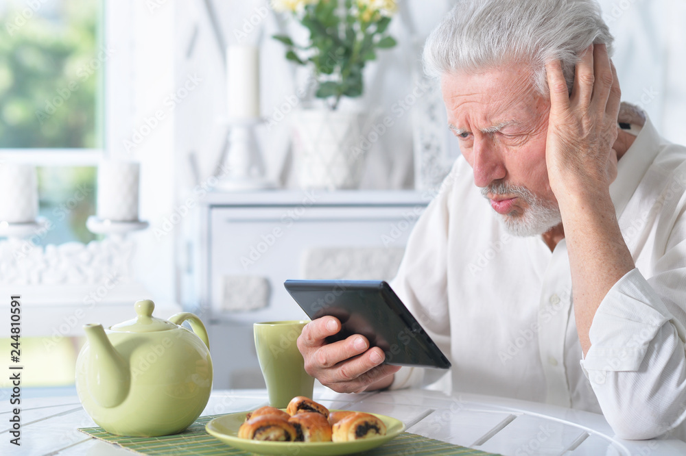 senior man using tablet while drinking tea senior man using tablet while drinking tea