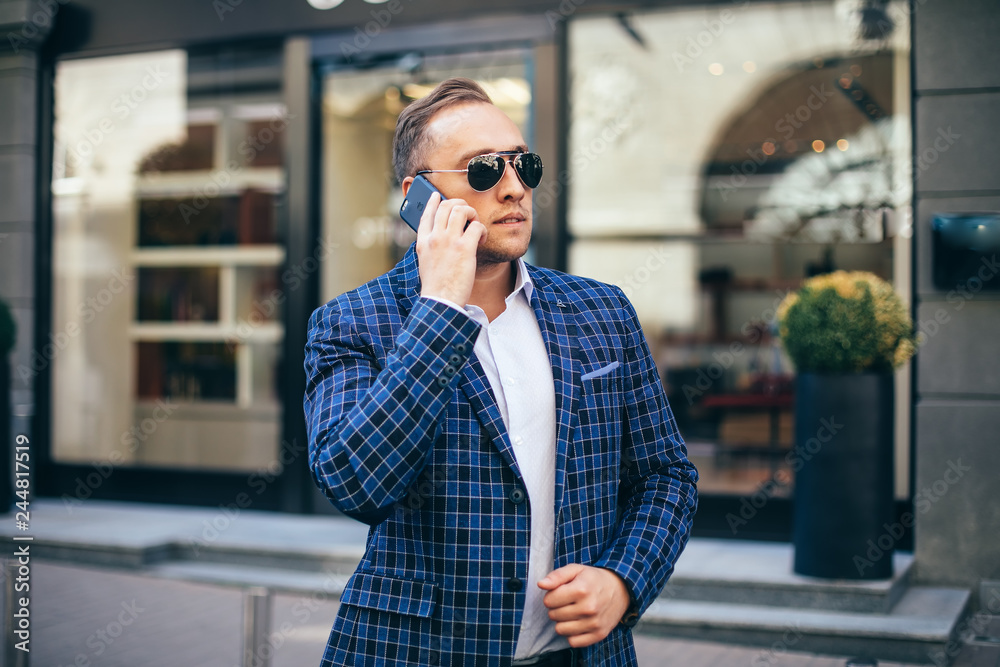 Portrait of stylish handsome young man with bristle standing outdoors. Man wearing jacket and shirt. man using mobile phone