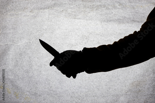 The knife in the hand of men who is ready to attack his victim. Breaking the law and crime. Attack with a knife. Silhouette on a light background.