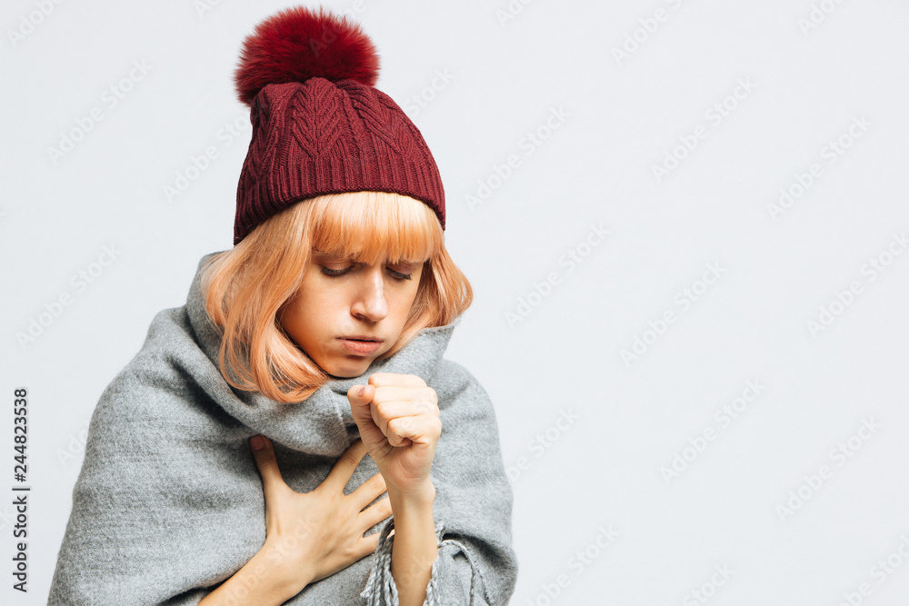 Cute sick young teen woman in red hat, wrapped in warm scarf coughing