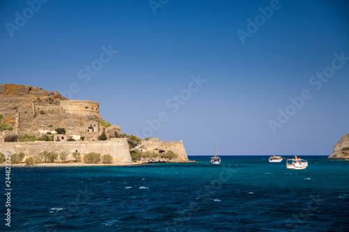 Cruise to the island of Spinalonga. Small boat on the blue lagoon. Spinalonga fortress on the island of Crete, Greece. Architecture on the island.