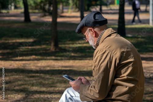Old man sitting on the bench, with a smartphone
