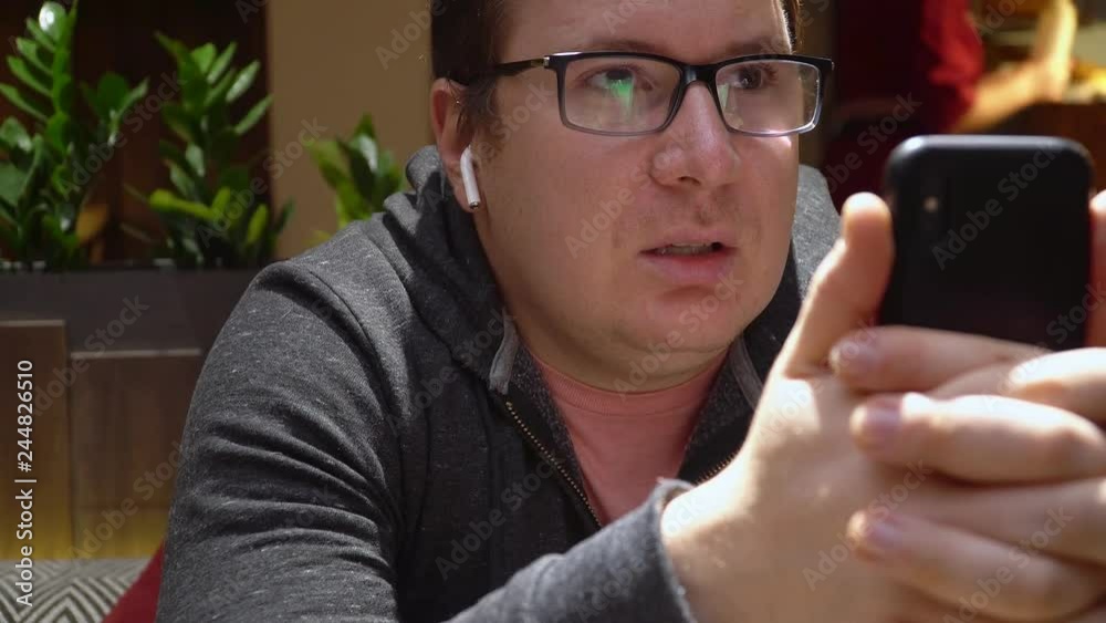 Man Make Online Video Call Using phone and wireless earpnones in restaurant blogger freelancer Man Make Online Video Call Using phone and wireless earpnones in restaurant blogger freelancer