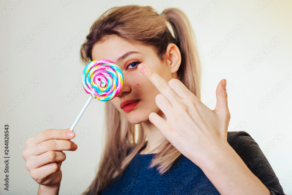 Portrait of attractive girl with colored, sweet candy shows gesture fuck off. The concept of greed.