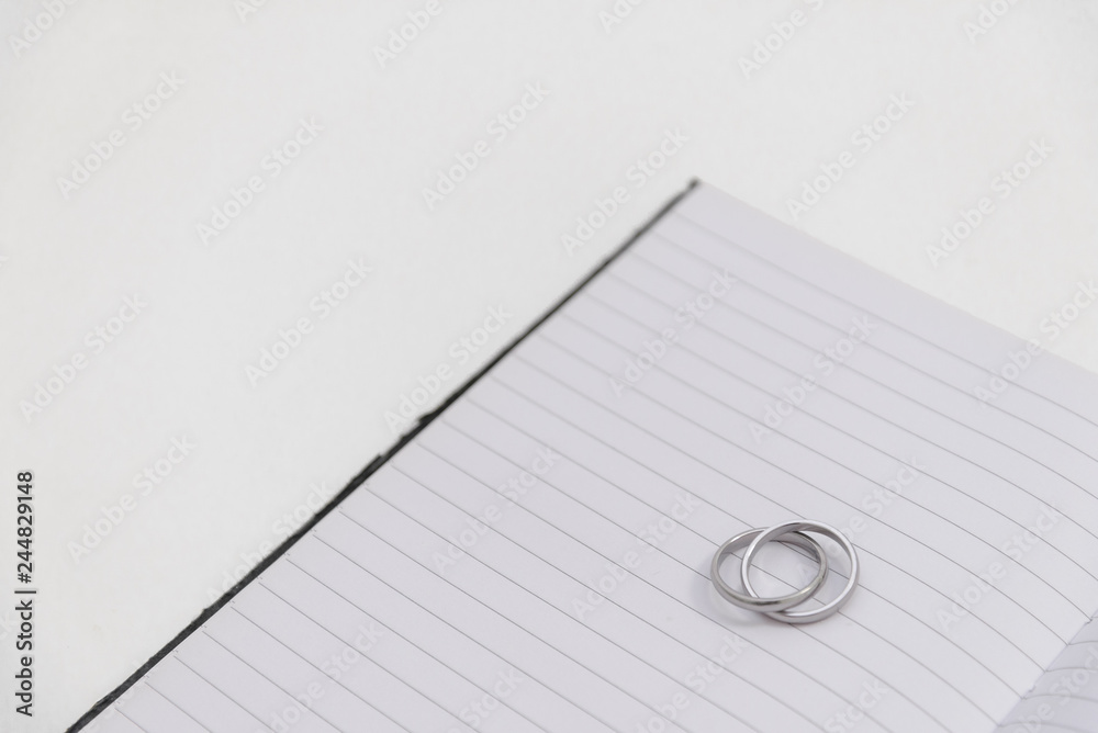 Crossing white gold or silver ring on lined paper notebook lie on white table background. Crossing white gold or silver ring on lined paper notebook lie on white table background.