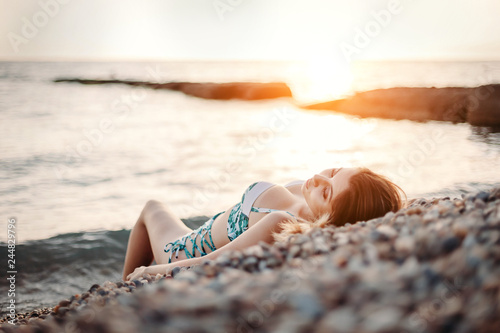Fashion shot of a beautiful happy girl in bikini lying on beach