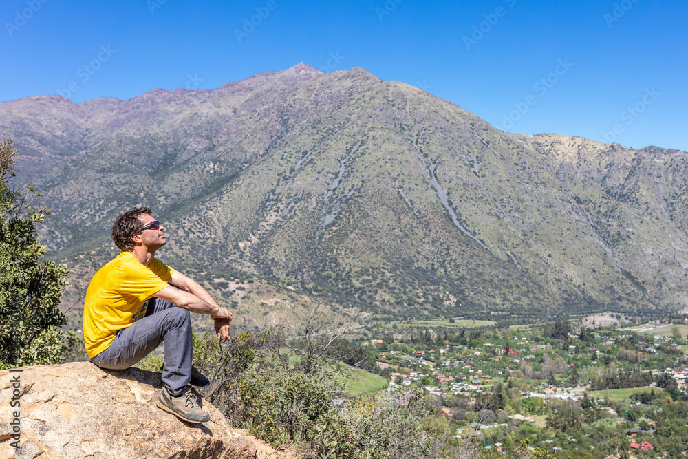 Naklejka premium A trekking man observes the infinity mountain landscape at Cajon del Maipo valley inside central Andes mountains at Santiago de Chile. An amazing scenery to enjoy and look at the view while hiking